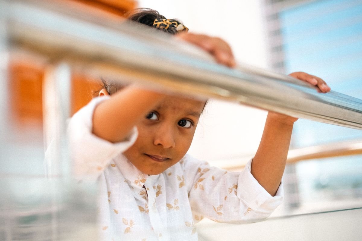 Menina segurando o corrimão em uma varanda de apartamento com vista urbana